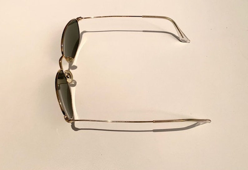 Peut inclure: Lunettes de soleil en m&eacute;tal dor&eacute; avec des verres vert fonc&eacute;. Les lunettes ont une monture fine en m&eacute;tal et sont de style classique.