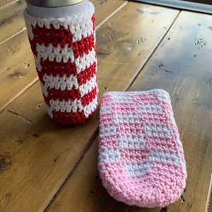 Puede incluir: Dos calientavasos de ganchillo, uno con rayas rojas y blancas y otro con rayas rosas y blancas.