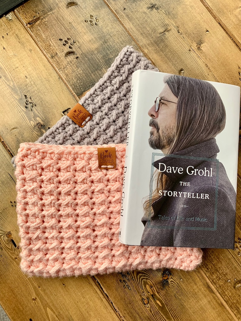 May include: Two crocheted neck warmers in pink and gray with leather tags that say "Book Lover". A book titled "Dave Grohl: The Storyteller" is on top of the warmers.