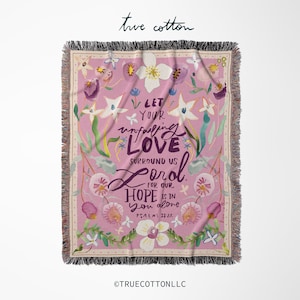 May include: A pink woven throw blanket with a floral pattern and the text "Let your unfailing love surround us Lord for our hope is in you alone. Psalm 33:22"