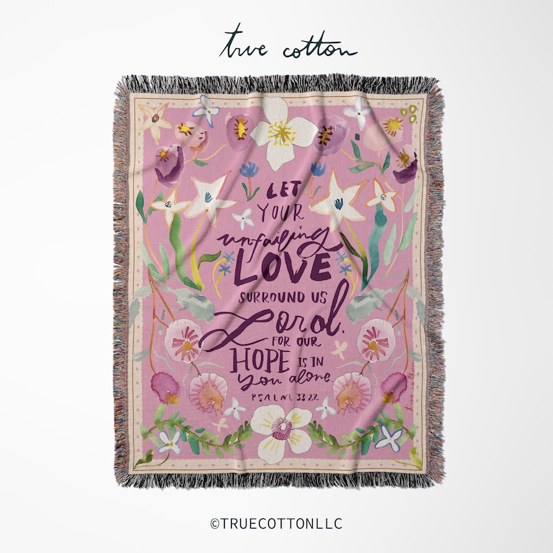 May include: A pink woven throw blanket with a floral pattern and the text "Let your unfailing love surround us Lord for our hope is in you alone. Psalm 33:22"
