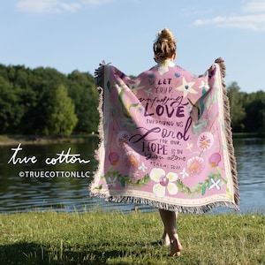 May include: A pink woven throw blanket with a floral design and the text "Let your unfailing love surround us Lord for our hope is in you alone Psalm 33:22".