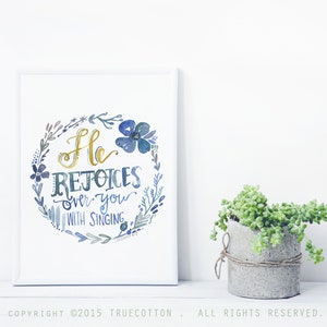 May include: A watercolor print with a blue and gold floral wreath and the text "He rejoices over you with singing".