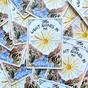 May include: A set of colorful stickers with a sun, river, and text that reads "The Light Shines In The Darkness But The Sun Has Not Overcome It."