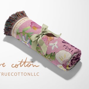 May include: A pink woven throw blanket with a floral pattern and the text "Just Breathe" in a script font. The blanket is rolled up and tied with a green ribbon.