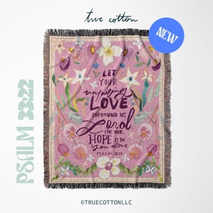 May include: A pink woven throw blanket with a floral design and the text "Let your unfailing love surround us Lord, for our hope is in you alone. Psalm 33:22."