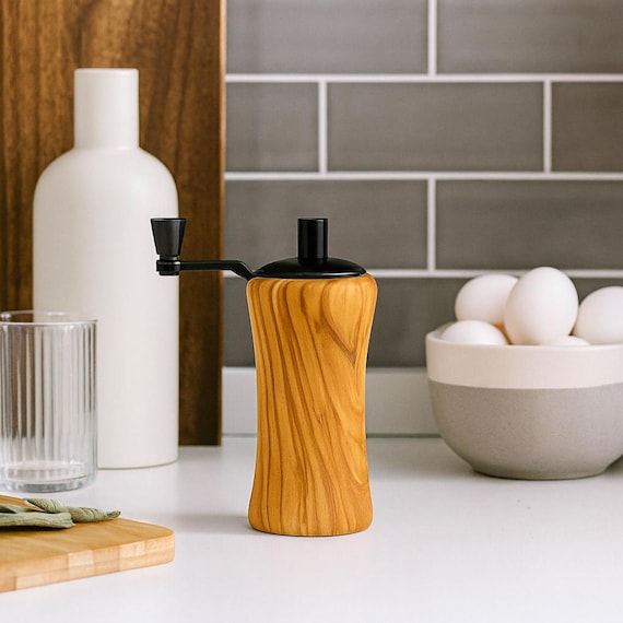 A miniature pepper grinder turned from actual olivewood — the grain patterns are one-of-a-kind and it's a genuinely artisan kitchen object you won't find at Williams Sonoma.