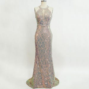 May include: A silver sequined halter-style evening gown with a beaded belt. The gown has a fitted silhouette and a mermaid skirt.