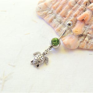 May include: A silver belly button ring with a green gem and a silver turtle charm.