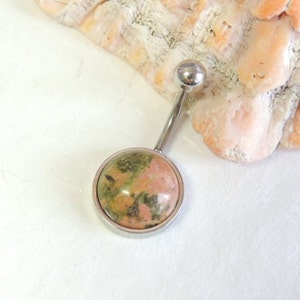 May include: A silver belly button ring with a round pink and green stone.