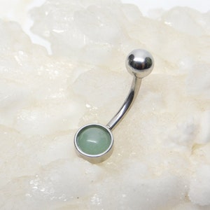 May include: A silver belly button ring with a round, light green gemstone.
