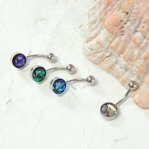 May include: Four belly button rings with different colored abalone shell accents. The rings are silver and have a curved bar.