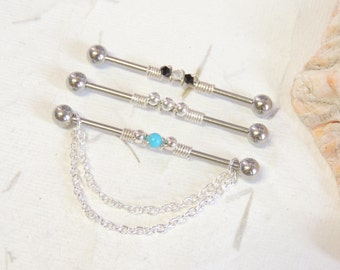 May include: Three silver barbell piercings with decorative beads and a chain. The top barbell has black and clear beads, the middle barbell has silver beads and a turquoise bead, and the bottom barbell has a silver chain.