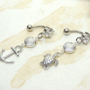 May include: Two silver belly button rings with charms. One ring has a seashell, a turtle, and an anchor charm. The other ring has a seashell and a clear crystal charm.