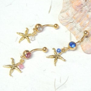 May include: Three gold belly button rings with a starfish charm and a crystal dangle. The charms are clear, pink, and blue.