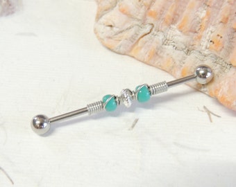May include: A silver barbell with turquoise beads and silver wire wraps. The barbell is on a white surface.