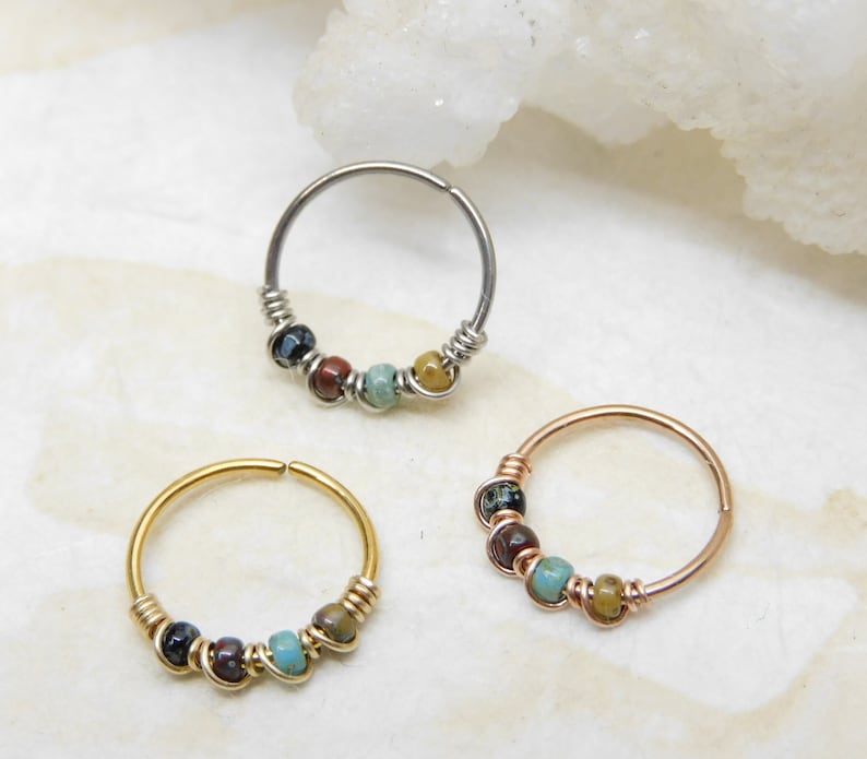 May include: Three hoop earrings with colourful beads. The hoops are made of silver, gold, and rose gold. The beads are a mix of turquoise, brown, and black.