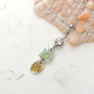 May include: A silver belly button ring with a clear crystal charm and a dangling pineapple charm with green glitter leaves and a yellow glitter pineapple.