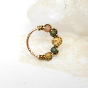 May include: A copper-colored nose ring with a series of colorful beads. The beads include pink, green, and yellow hues, and are strung together with wire. The ring is designed to be worn in the nose.