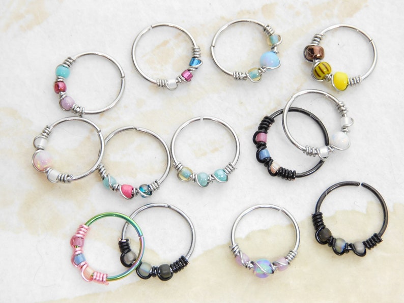 May include: A collection of 12 silver and black hoop earrings with various coloured beads and charms. The earrings are all different designs and feature a variety of colours, including pink, blue, green, yellow, and white.