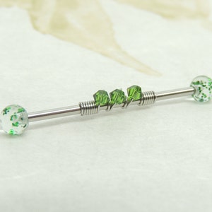 May include: A silver barbell with green glitter balls and green crystal accents. The barbell is a body piercing jewelry item.