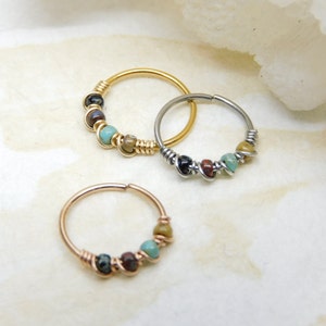 May include: Three nose rings with colourful beads. The rings are made of gold, silver, and rose gold. The beads are turquoise, brown, and black.