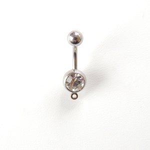 May include: A silver belly button ring with a clear crystal in the center.