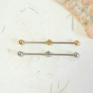 May include: Two surgical steel barbell body jewelry pieces with star-shaped charms. The top barbell is gold-toned and the bottom barbell is silver-toned.