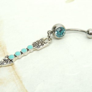 May include: A silver belly button ring with a turquoise blue gem and a dangling arrow charm with turquoise blue accents.