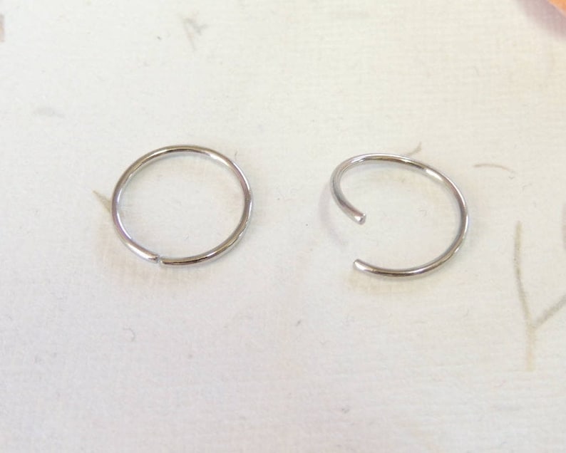 May include: Two silver hoop earrings, one is open and the other is closed.