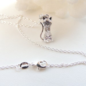 Puede incluir: Un collar plateado con un colgante de gato adornado con piedras preciosas transparentes. El colgante de gato est&aacute; dise&ntilde;ado con cabeza, cuerpo y cola. La delicada cadena tiene un cierre de mosquet&oacute;n. El colgante mide aproximadamente 2,5 cm de altura.