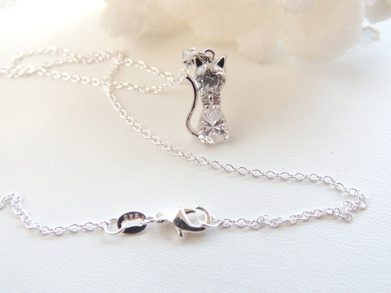 Puede incluir: Un collar plateado con un colgante de gato adornado con piedras preciosas transparentes. El colgante de gato est&aacute; dise&ntilde;ado con cabeza, cuerpo y cola. La delicada cadena tiene un cierre de mosquet&oacute;n. El colgante mide aproximadamente 2,5 cm de altura.