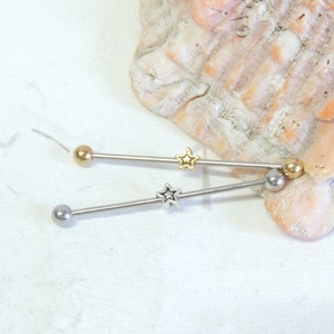 May include: Two silver barbell style body jewelry pieces with gold star accents. The jewelry is on a white background.