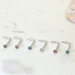 May include: Seven silver nose rings with different colored gemstones. The gemstones are blue, clear, red, and green.