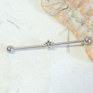 May include: Silver barbell with a star charm in the center. The barbell is a body piercing jewelry item.