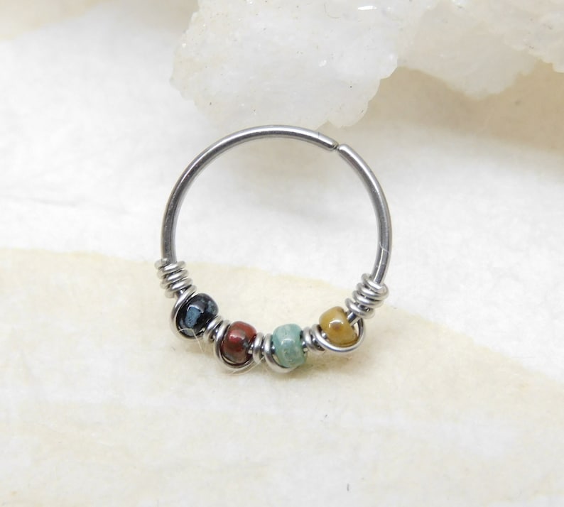 May include: A silver hoop earring with a beaded design. The beads are in shades of black, brown, green, and yellow.