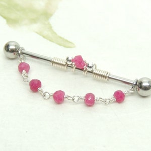 May include: A silver barbell with a pink gemstone chain. The barbell has two silver balls on the ends and a silver spring in the middle. The chain has several pink gemstones.