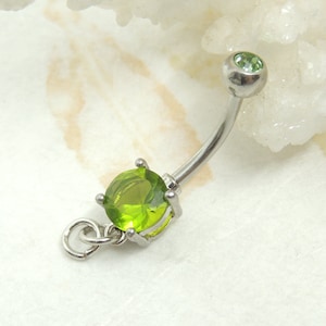 May include: A curved belly button ring with a silver-colored metal finish. The ring features a large, round, light green gemstone at the bottom and a smaller, matching gemstone at the top. A small loop hangs from the larger gemstone.