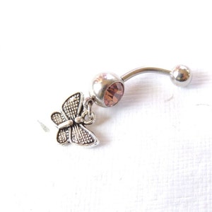 May include: A silver belly button ring with a clear, light brown gem and a silver butterfly charm.