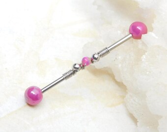 May include: A silver industrial barbell with pink accents. The barbell features a long, straight bar with a pink ball on each end. The center of the barbell has small pink beads and silver detailing.