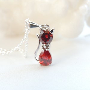 Puede incluir: Collar con colgante de gato de plata. El colgante tiene forma de gato con dos piedras rojas, una ovalada y otra en forma de l&aacute;grima. El dise&ntilde;o del collar es sencillo y elegante.