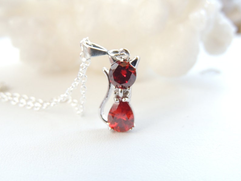 Puede incluir: Collar con colgante de gato de plata. El colgante tiene forma de gato con dos piedras rojas, una ovalada y otra en forma de l&aacute;grima. El dise&ntilde;o del collar es sencillo y elegante.