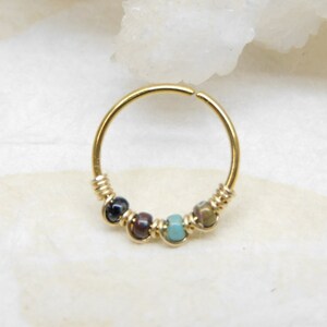 May include: Gold hoop earring with a row of colourful beads. The beads are a mix of blue, green, brown, and black.