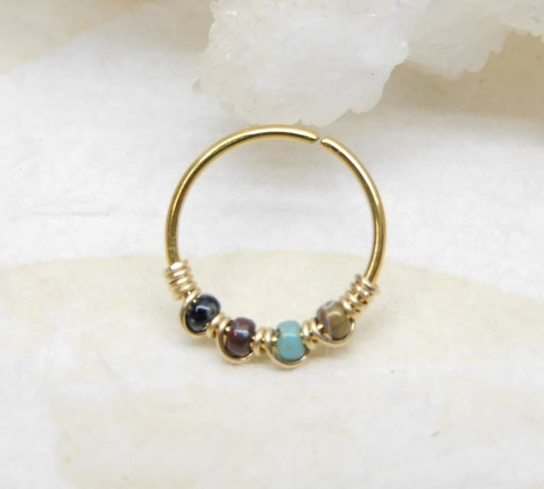 May include: Gold hoop earring with a row of colourful beads. The beads are a mix of blue, green, brown, and black.