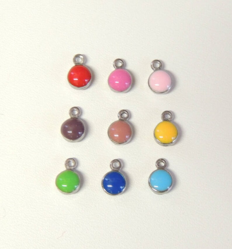 May include: Nine colourful round charms with silver-tone metal loops. The charms are in various colours, including red, pink, light pink, brown, peach, yellow, green, blue, and turquoise. Each charm has a glossy finish.