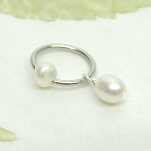 May include: A silver hoop earring with a white pearl dangling from the bottom and a white pearl on the hoop.