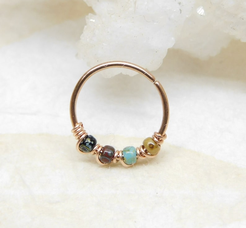 May include: A gold hoop earring with a beaded design. The beads are brown, black, turquoise, and green.
