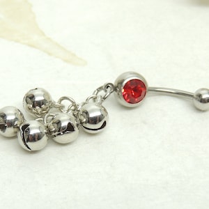 May include: Silver belly button ring with a red gem and a cluster of five silver bells dangling from it.