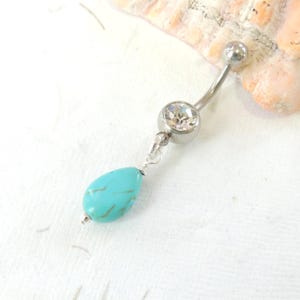 May include: A silver belly button ring with a clear crystal and a turquoise dangle charm.