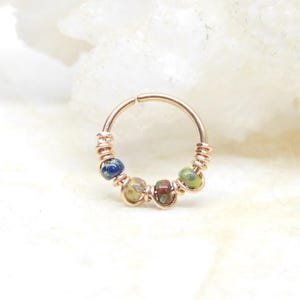 May include: A rose gold hoop earring with a beaded design. The beads are a mix of blue, green, and brown.